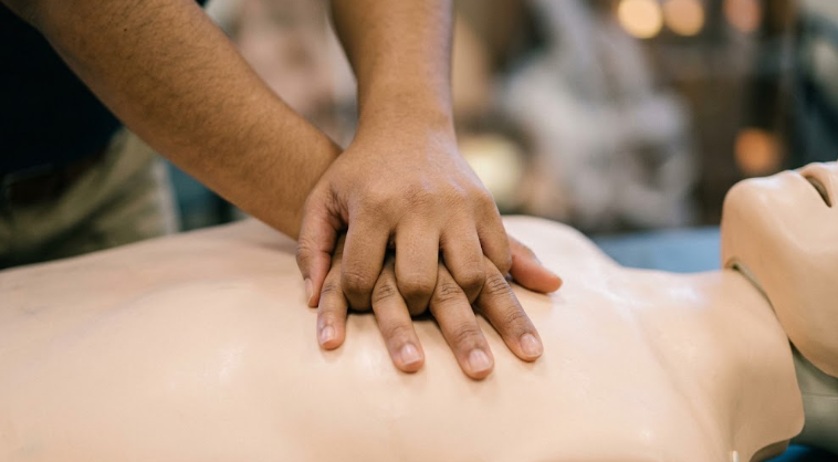 Hands performing CPR chest compressions on a training mannequin during a corporate safety training course.