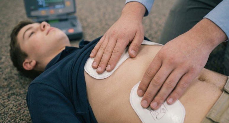 Rescuer placing electrode pads on young person's bare torso.